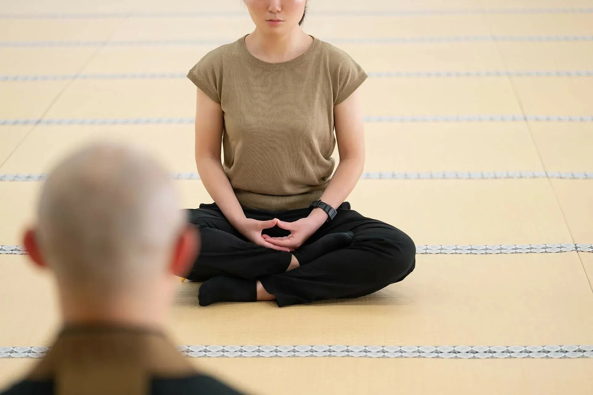 A person sitting zazen in the cosmic mudra, a teacher keeping watch nearby